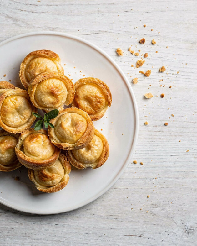 A golden brown pastel de marias broken open on a rustic wooden board, revealing its savory filling.