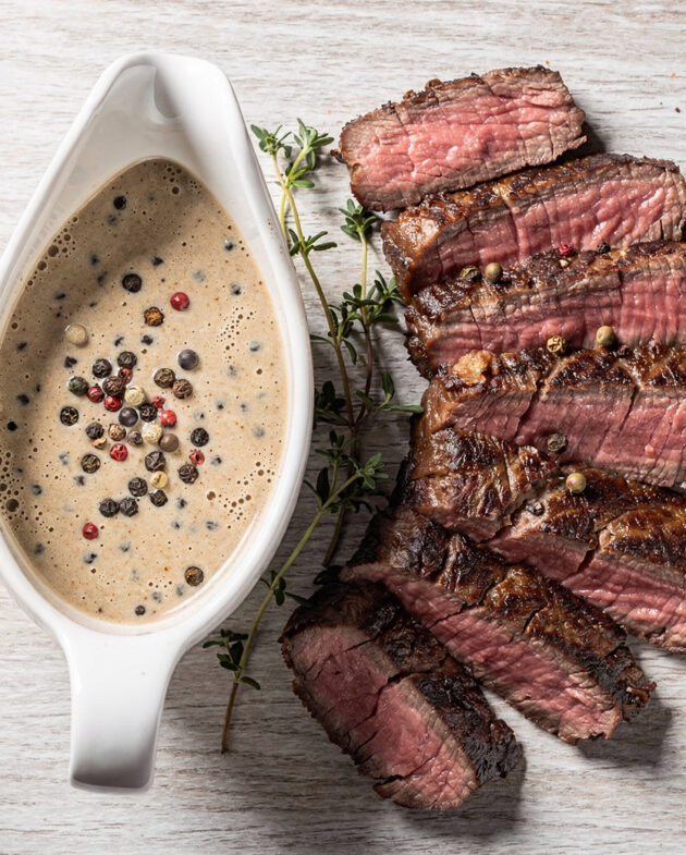 A glossy, creamy peppercorn steak sauce drizzled over a perfectly seared steak, with visible cracked black peppercorns.
