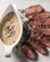 A glossy, creamy peppercorn steak sauce drizzled over a perfectly seared steak, with visible cracked black peppercorns.
