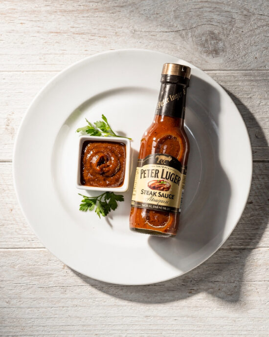 A rich, glossy homemade peter luger steak sauce drizzled over a perfectly grilled steak on a wooden board.