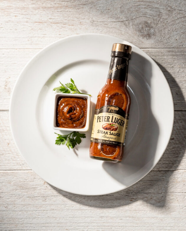 A rich, glossy homemade peter luger steak sauce drizzled over a perfectly grilled steak on a wooden board.