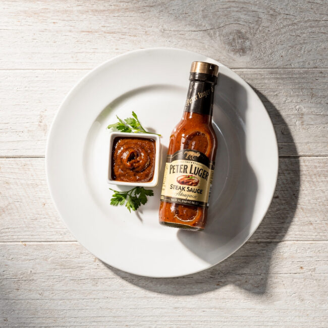 A rich, glossy homemade peter luger steak sauce drizzled over a perfectly grilled steak on a wooden board.