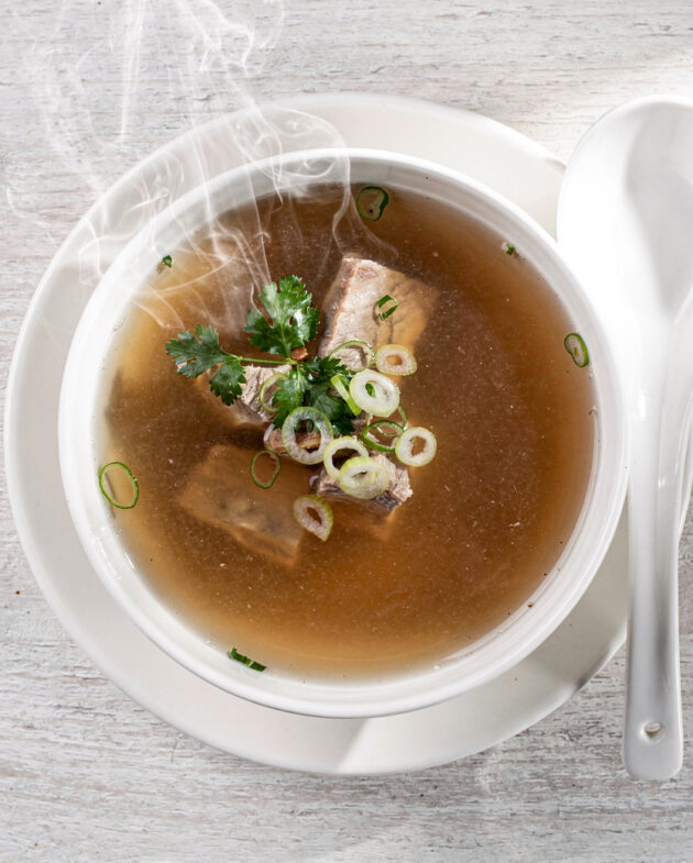 A rich, amber-hued pork bone broth served in a simple white bowl, garnished with fresh chives.