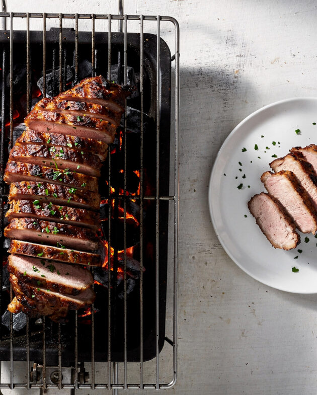 Slices of perfectly cooked pork loin on charcoal grill rest on a wooden cutting board, ready to serve.