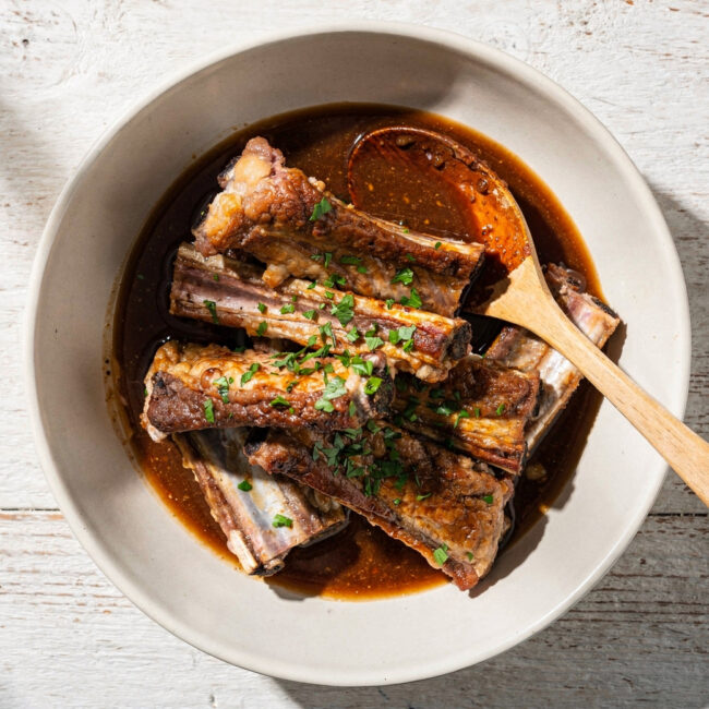 A bowl of rich, dark pork ribs marinade sits ready to transform a rack of ribs on a rustic wooden table.