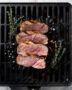 A beautifully grilled pork tenderloin on charcoal grill, sliced and served on a wooden platter.