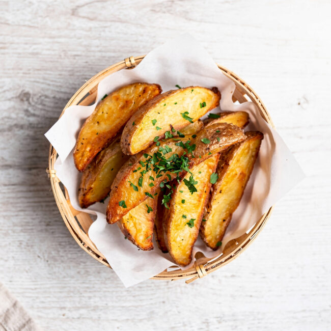 A heaping basket of golden brown potato wedges sprinkled with parsley, ready for dipping.