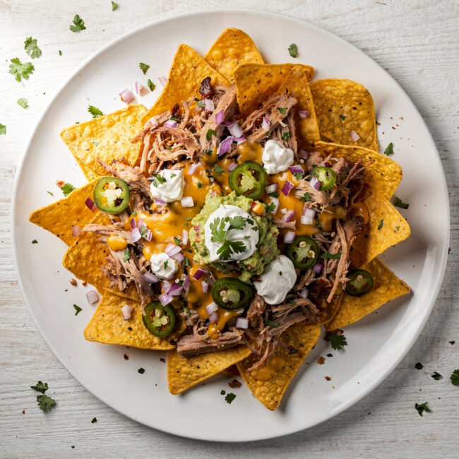 A close-up, overhead shot of the ultimate pulled pork nachos recipe, featuring melty cheese, tender meat, and fresh garnishes.