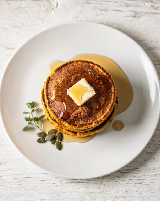 A golden stack of fluffy pumpkin pancake recipe drizzled with maple syrup on a rustic wooden table.