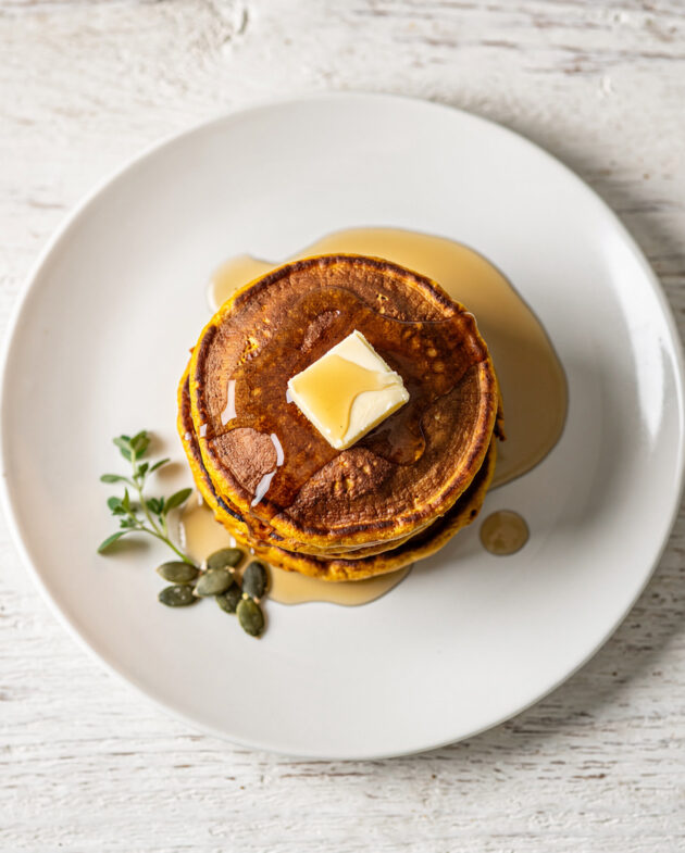A golden stack of fluffy pumpkin pancake recipe drizzled with maple syrup on a rustic wooden table.