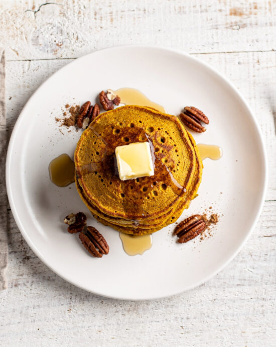 A golden stack of fluffy pumpkin pancakes from this classic pumpkin pancake recipe, drizzled with maple syrup.
