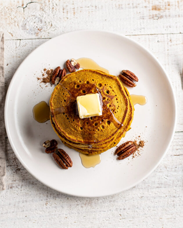 A golden stack of fluffy pumpkin pancakes from this classic pumpkin pancake recipe, drizzled with maple syrup.