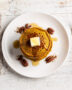 A golden stack of fluffy pumpkin pancakes from this classic pumpkin pancake recipe, drizzled with maple syrup.