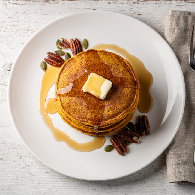 A golden stack of fluffy pumpkin pancakes drizzled with maple syrup, showcasing the perfect execution of this pumpkin pancake recipe.