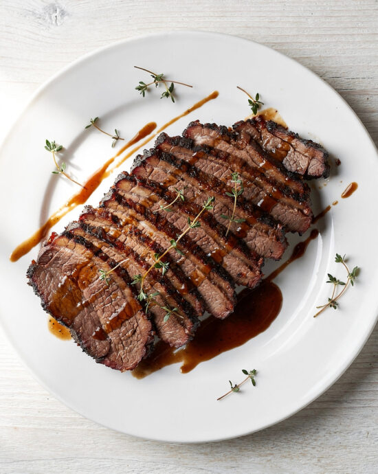 A perfectly cooked roasted brisket recipe, sliced and glistening with savory juices on a wooden board.