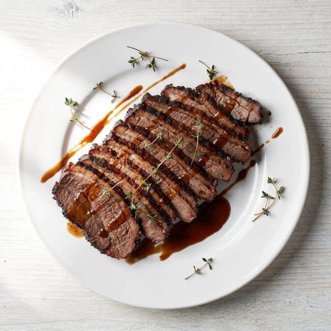 A perfectly cooked roasted brisket recipe, sliced and glistening with savory juices on a wooden board.