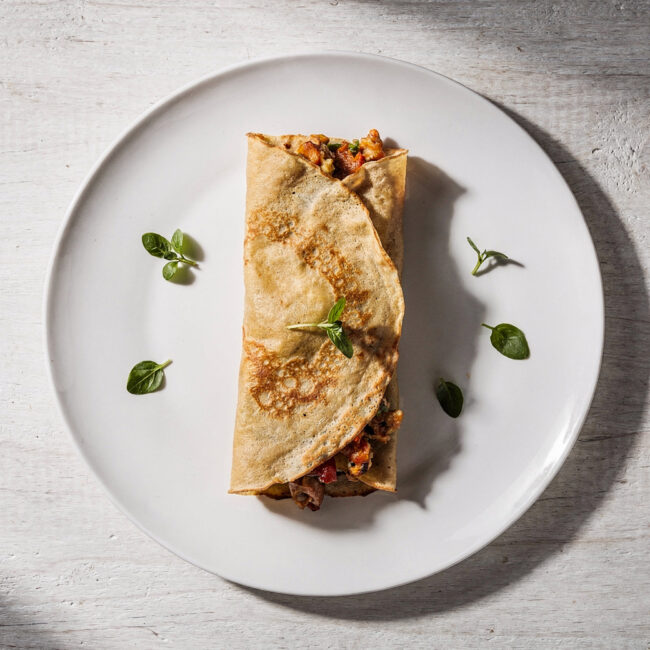 A beautifully plated savory crepe recipe with golden edges, oozing with cheese and béchamel sauce.