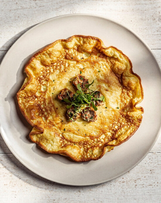 A golden, puffy savory Dutch pancake recipe with a crispy potato crust, fresh herbs, and sour cream on a wooden board.