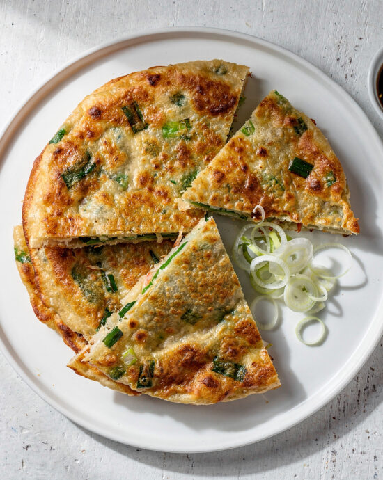 A stack of golden-brown scallion pancakes on a rustic wooden board, showcasing their flaky layers.