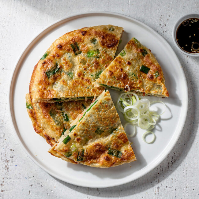 A stack of golden-brown scallion pancakes on a rustic wooden board, showcasing their flaky layers.