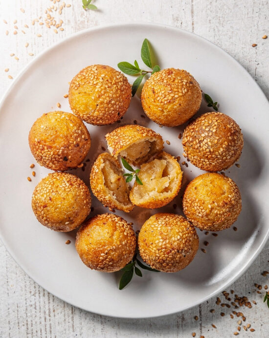 A rustic pile of golden-brown homemade sesame balls with a perfectly cracked, seed-covered exterior, ready to be devoured.