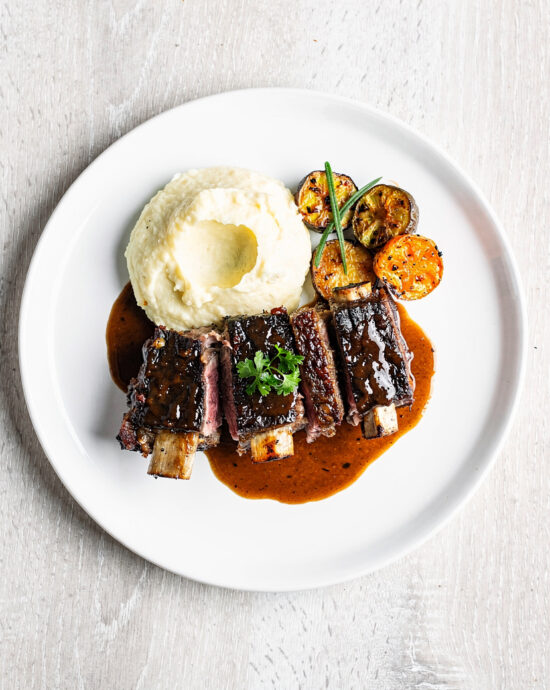A beautifully plated short ribs recipe with the tender meat falling off the bone, served over creamy mashed potatoes.