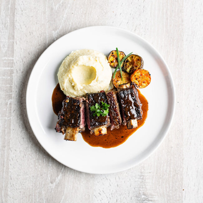 A beautifully plated short ribs recipe with the tender meat falling off the bone, served over creamy mashed potatoes.