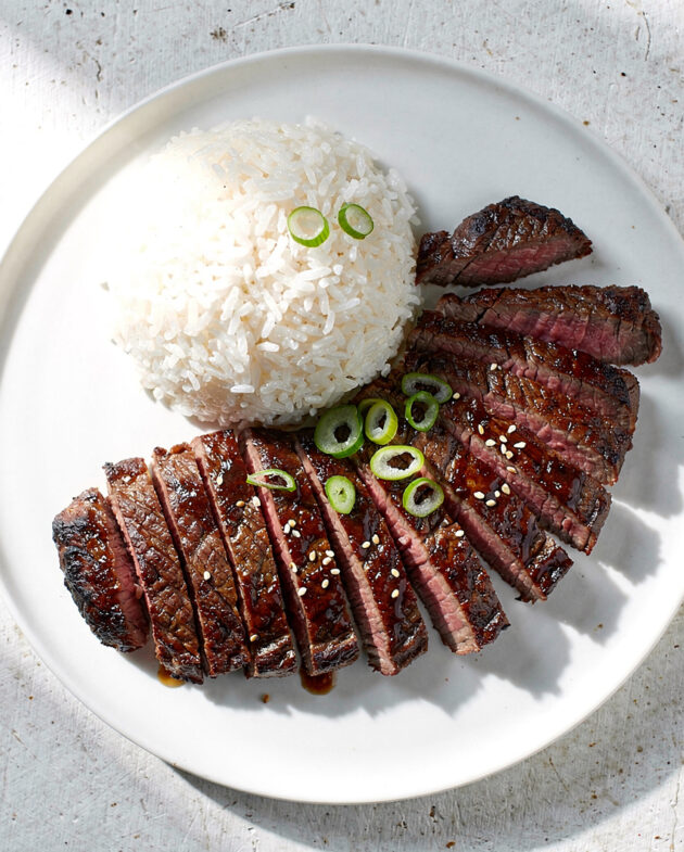 Perfectly grilled slices of skirt steak asian marinade, showing a caramelized crust and juicy pink interior, plated simply.