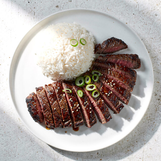 Perfectly grilled slices of skirt steak asian marinade, showing a caramelized crust and juicy pink interior, plated simply.