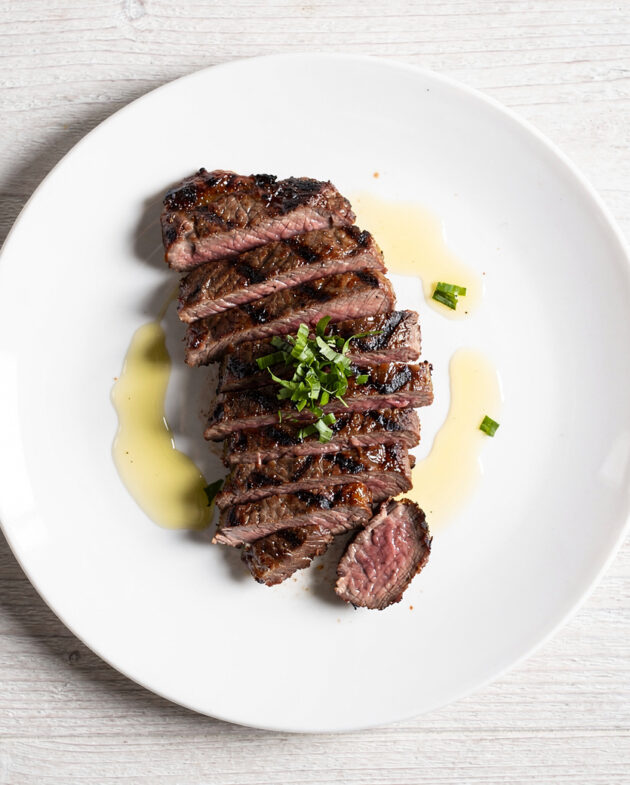 A beautifully plated skirt steak churrasco sliced against the grain, drizzled with vibrant green chimichurri sauce.