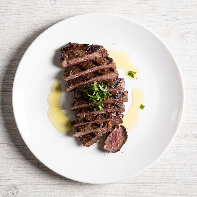 A beautifully plated skirt steak churrasco sliced against the grain, drizzled with vibrant green chimichurri sauce.