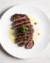 A beautifully plated skirt steak churrasco sliced against the grain, drizzled with vibrant green chimichurri sauce.