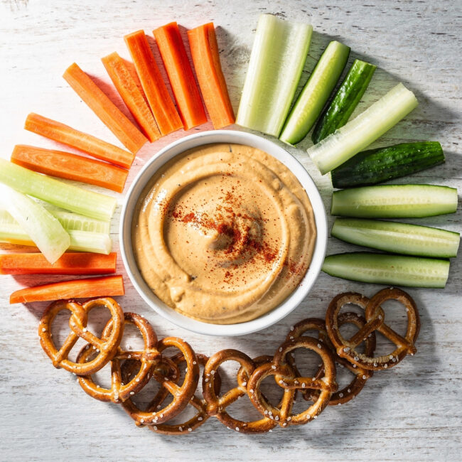 A creamy honey-mustard dip in a white bowl, surrounded by soft pretzels, perfect for quick snacks treats.