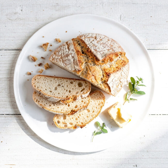 A rustic loaf of soda bread with buttermilk recipe sits on a wooden cutting board, warm from the oven.