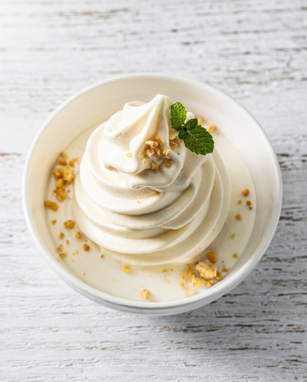 A perfectly swirled cone of homemade soft serve recipe with a vanilla bean speckled surface.