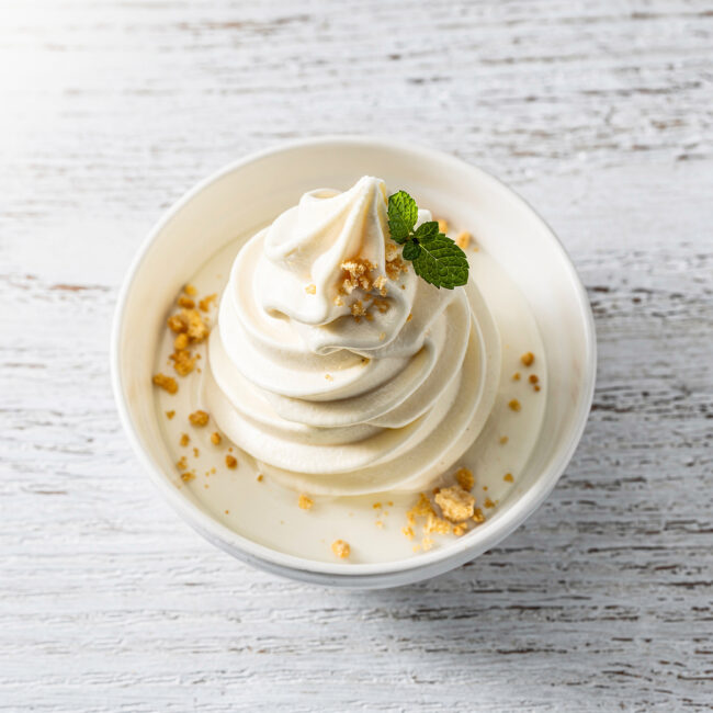 A perfectly swirled cone of homemade soft serve recipe with a vanilla bean speckled surface.