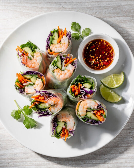 A top-down view of crispy homemade spring roll recipe plated on a rustic wooden board with dipping sauce.