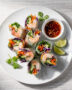A top-down view of crispy homemade spring roll recipe plated on a rustic wooden board with dipping sauce.
