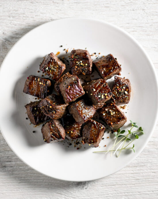 A close-up shot of savory steak bites coated in a rich, dark steak bites seasoning, ready to be seared.