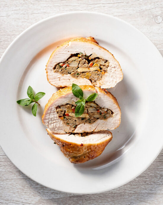 A golden-brown stuffed chicken breast with a creamy herbed filling, served on a white plate.