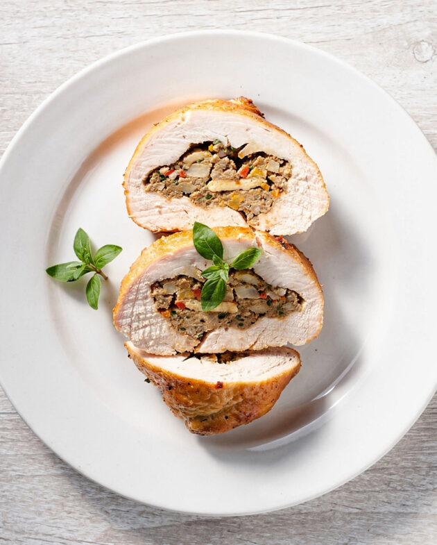 A golden-brown stuffed chicken breast with a creamy herbed filling, served on a white plate.
