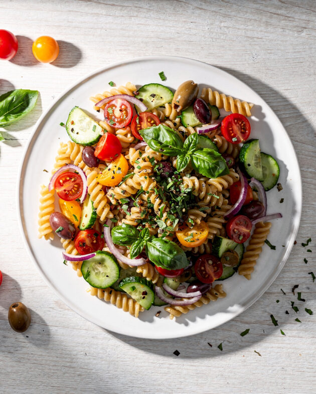 A vibrant summer pasta salad with colorful vegetables and fusilli pasta, beautifully plated on a light wood table.