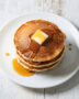 A stack of fluffy, golden pancakes from this sweet pancake recipe, drizzled with maple syrup, on a rustic wood table.