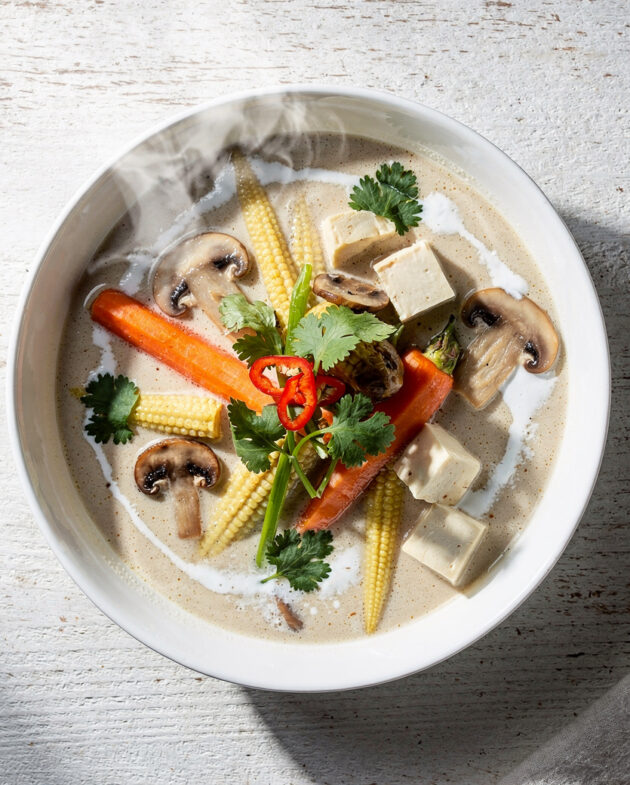A vibrant bowl of creamy tom kha vegetable soup garnished with cilantro and lime.