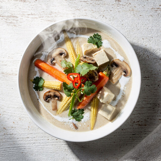 A vibrant bowl of creamy tom kha vegetable soup garnished with cilantro and lime.