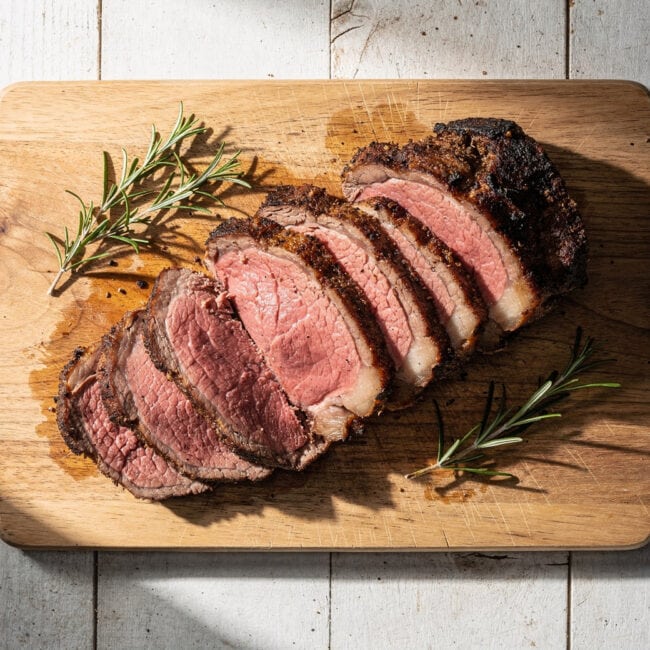 A perfectly cooked traeger boneless prime rib rests on a cutting board, showcasing a dark, peppery crust and a juicy pink interior.