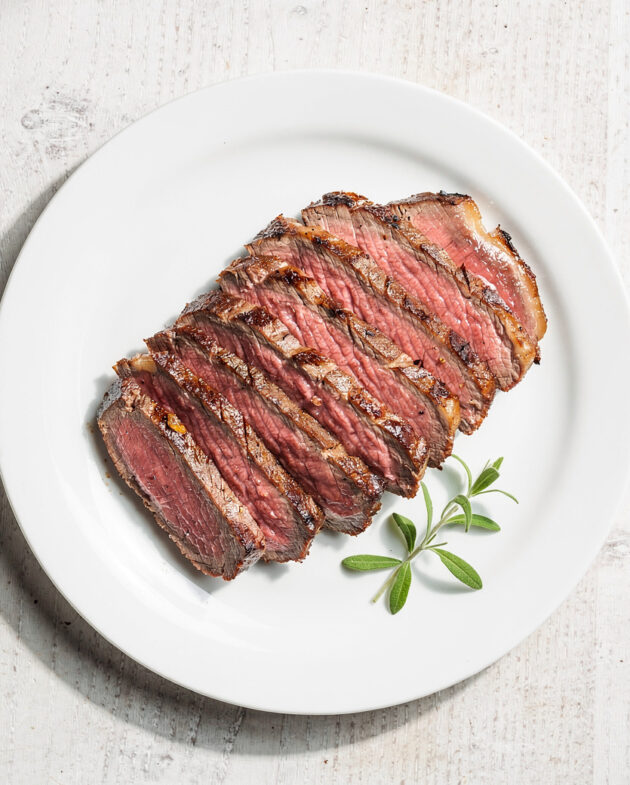 A beautifully grilled tri tip steak resting on a wooden cutting board, sliced to reveal a perfect pink interior.
