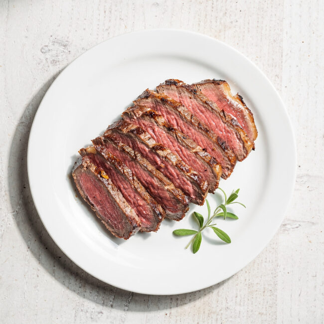 A beautifully grilled tri tip steak resting on a wooden cutting board, sliced to reveal a perfect pink interior.