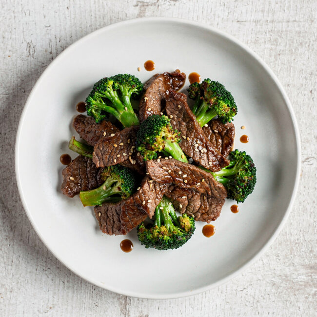 A steaming plate of the classic beef and broccoli recipe, featuring tender slices of beef and crisp broccoli in a glossy, savory sauce.