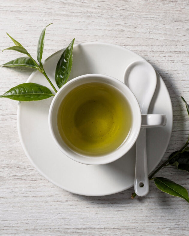 A jar of green tea chinese paste sits next to fresh ingredients on a rustic wooden table.